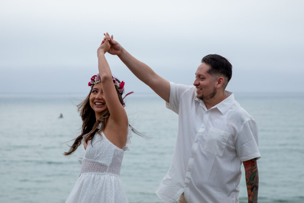 Engaged couple twirling on a cliffside in front of the ocean. 