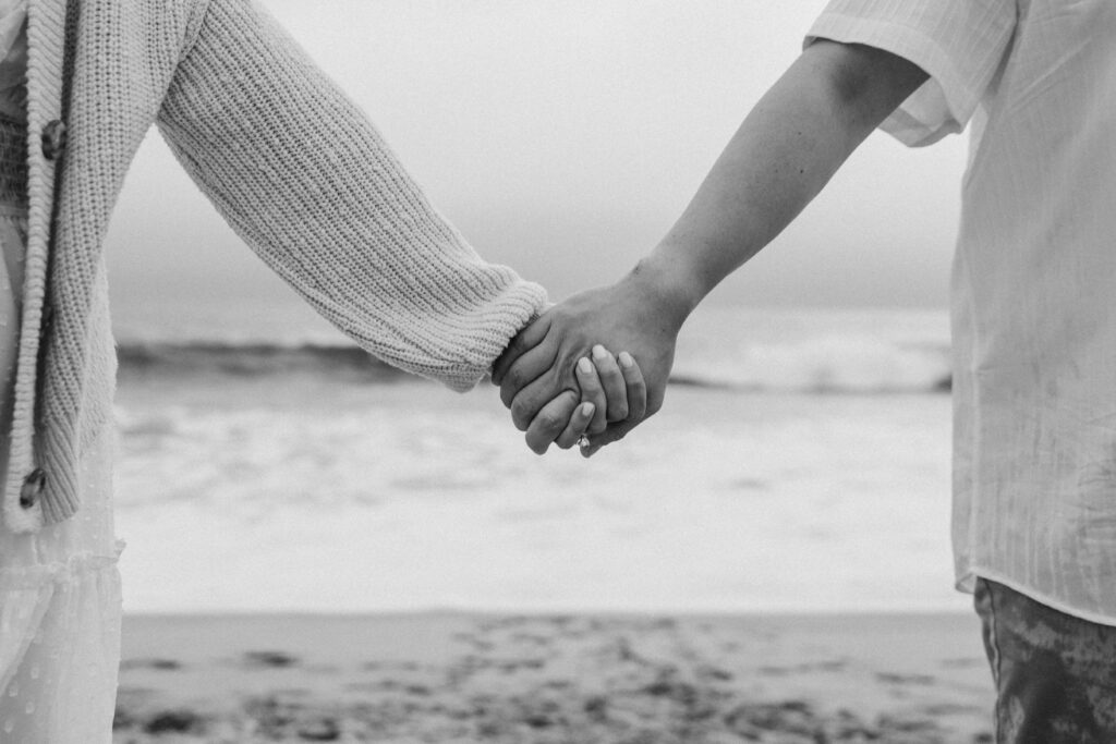 Engaged couple holding hands in front of the ocean. 