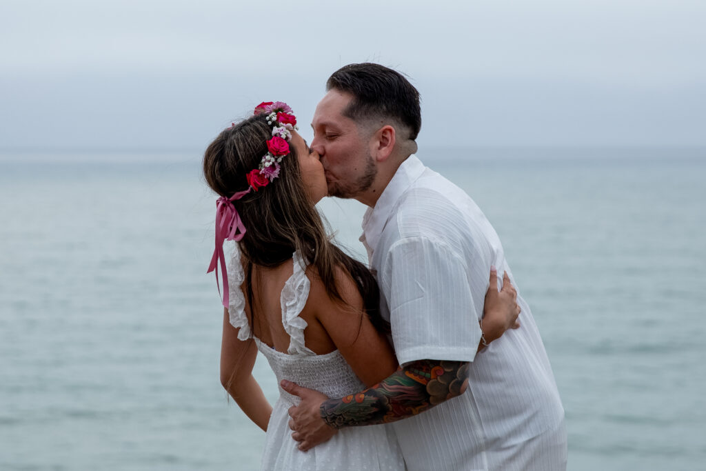 Engaged couple kissing on a cliffside in front of the ocean. 