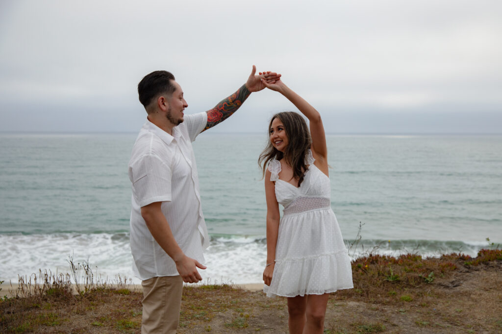 Beach engagement photos, with guy twirling girl on a cliffside in California. 