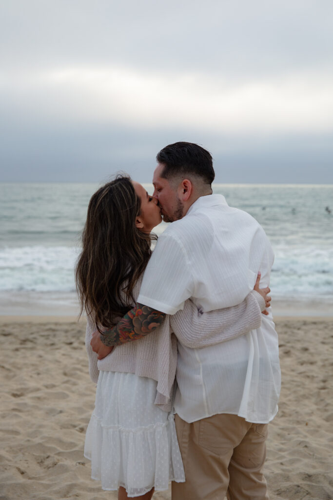 Engaged couple kissing on the beach in front of the ocean. 