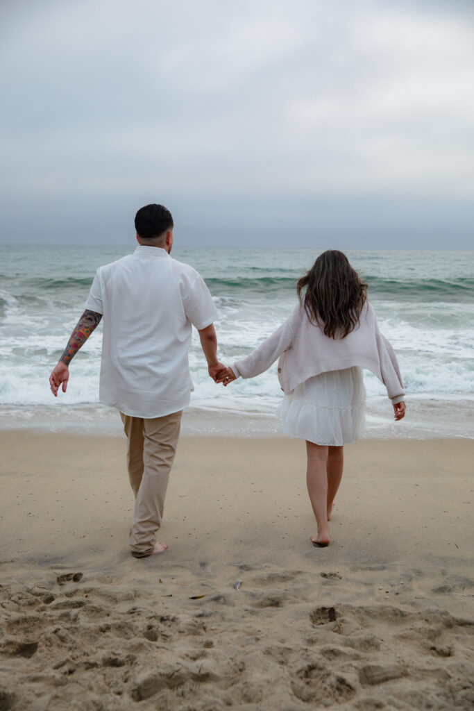 Guy and girl holding hands and walking on the beach.  