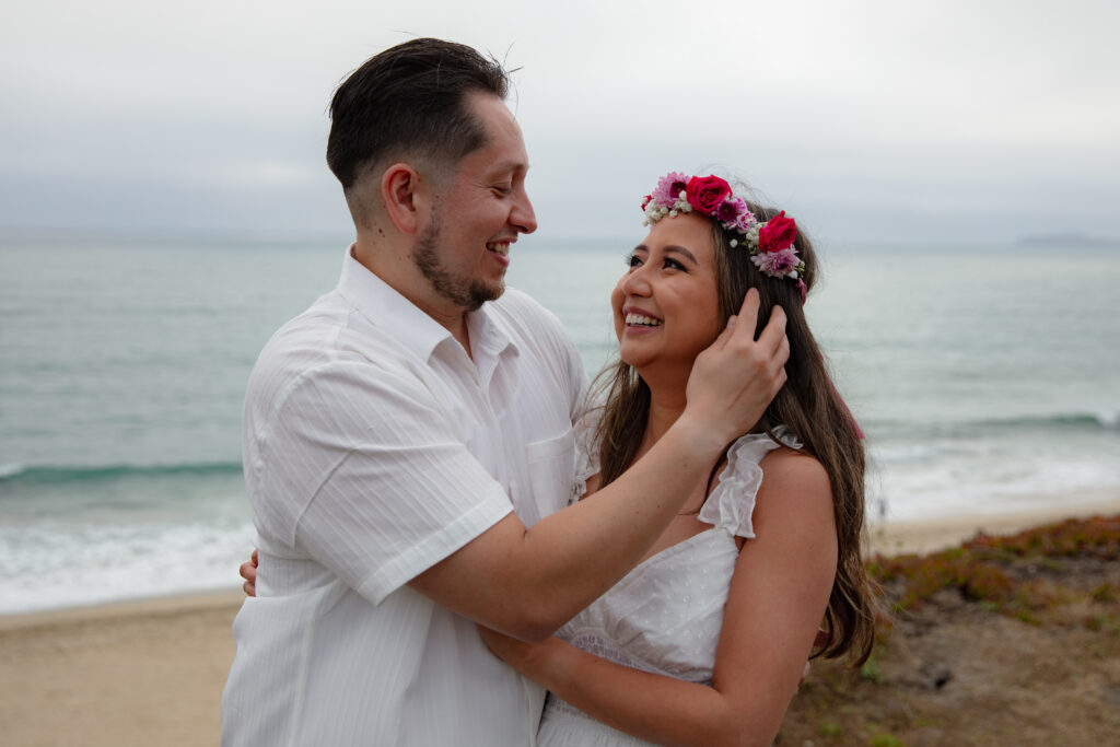 Man brushing Fiancee's hair on a cliffside in front of the ocean. 